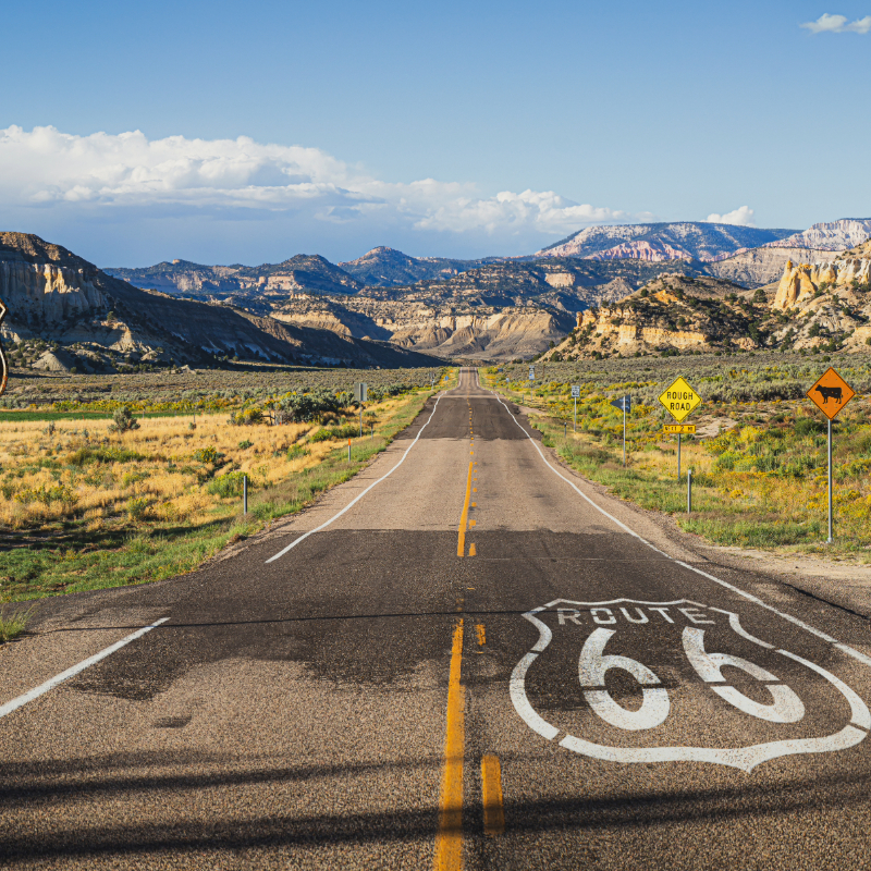 Straight Highway road leading towards the mountains in the backdrop. Route 66 symbol is painted white on the road