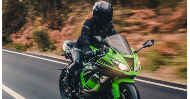 Woman in black gear riding green motorcycle